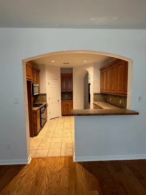 Archway opening to kitchen with wood-finish flooring, wood cabinetry, tile flooring, and a breakfast bar