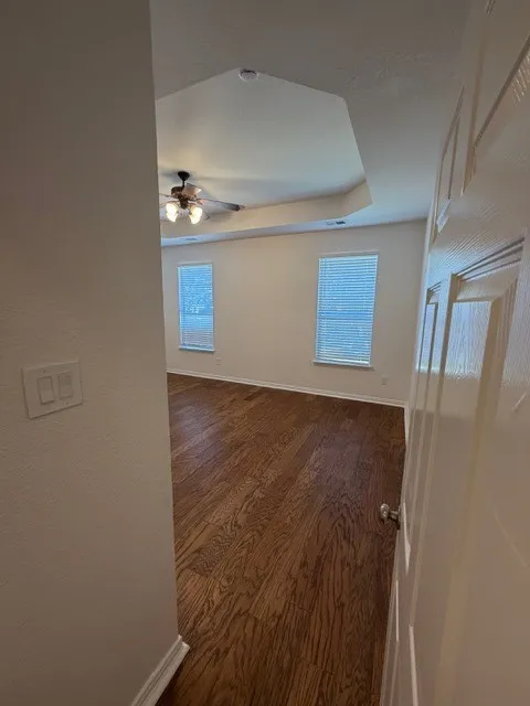 Tray ceiling with a ceiling fan, two windows with blinds, and wood-finish flooring