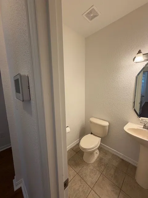 Pedestal sink with polished chrome fixtures, wall-mounted light fixture, and tile flooring