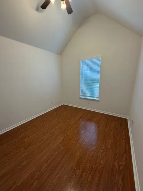 Vaulted ceiling with a ceiling fan, wood-finish flooring, and a window with blinds