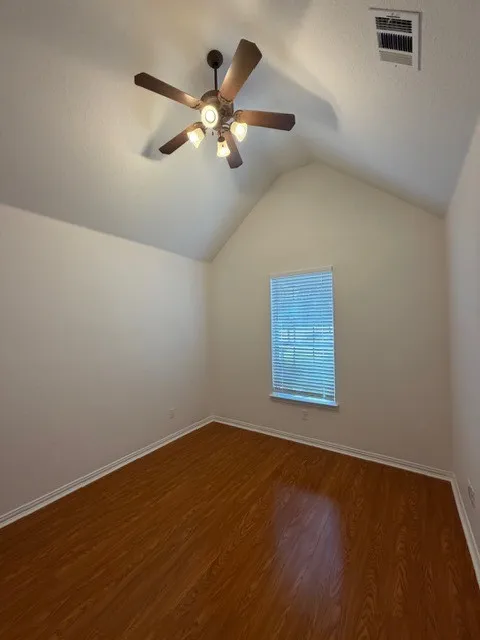 Spacious room featuring soaring vaulted ceilings, warm wood-finish flooring, and abundant natural light from a large window