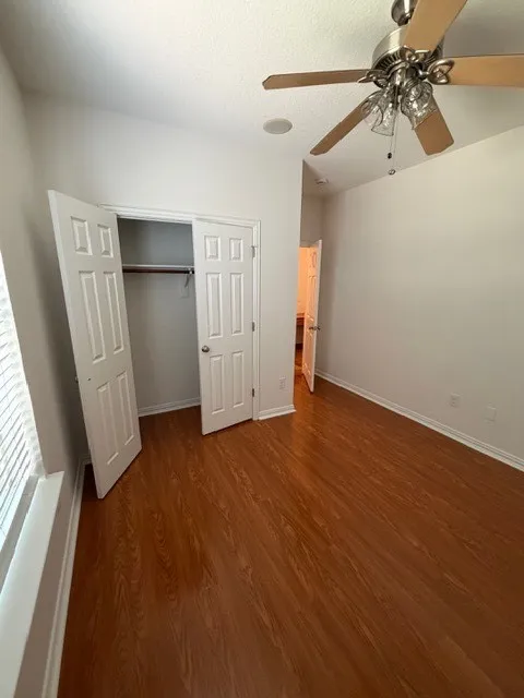 Wood-finish flooring, ceiling fan with integrated lighting, recessed ceiling speaker, bi-fold closet doors, and window with blinds