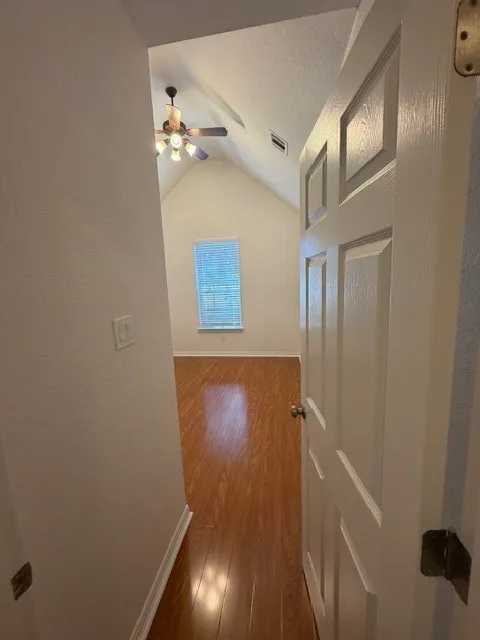Vaulted ceiling room with wood-finish flooring, a ceiling fan with light, and natural light from a window with blinds