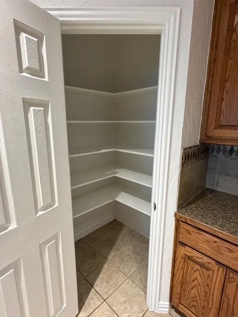 Walk-in pantry with extensive corner shelving, tile flooring, and a paneled door