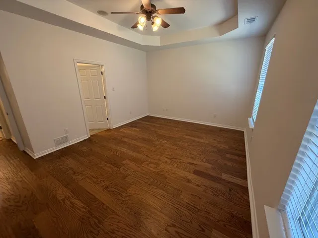 Tray ceiling with a ceiling fan light fixture, wood-finish flooring, and white window blinds