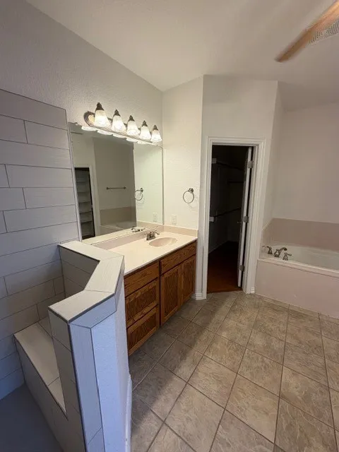 Dual vanity with wood-finish cabinetry, a large mirror, and overhead lighting