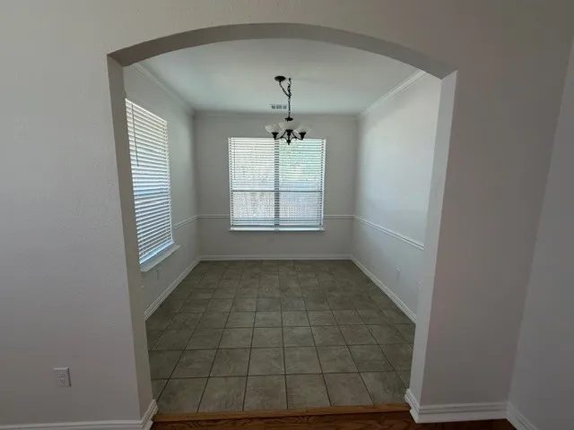 Arched entry to a room featuring tile flooring, dual windows with blinds, a chandelier, and crown molding