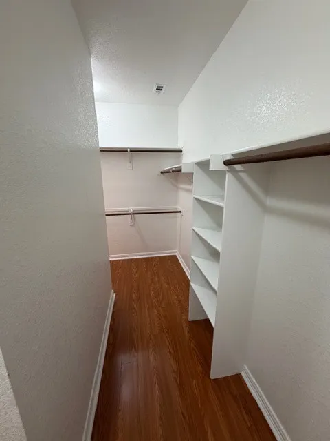 Walk-in closet with wood-finish flooring, white walls, built-in shelving, and multiple hanging rods