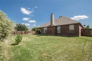 Expansive fenced backyard featuring a brick exterior, covered patio, and mature landscaping