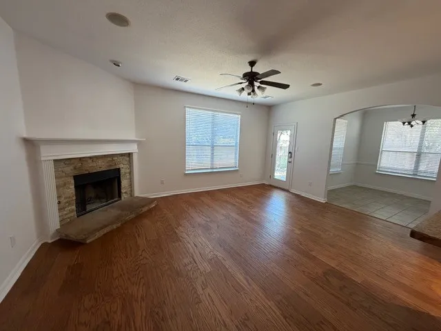 Wood-finish flooring throughout, stone-faced fireplace with a substantial hearth, ceiling fan with integrated lighting, recessed lighting, and an arched entryway to the adjoining space