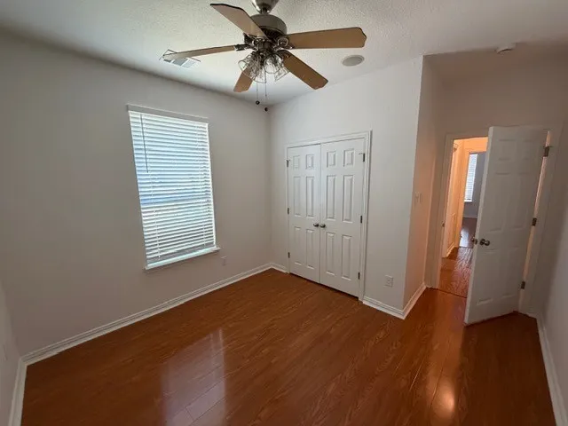 Wood-finish flooring with crisp white baseboards, a double-door closet, and a ceiling fan with integrated lighting