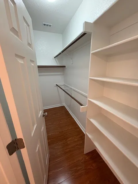White paneled door opening to a closet featuring wood-finish flooring, integrated shelving, and clothing rods