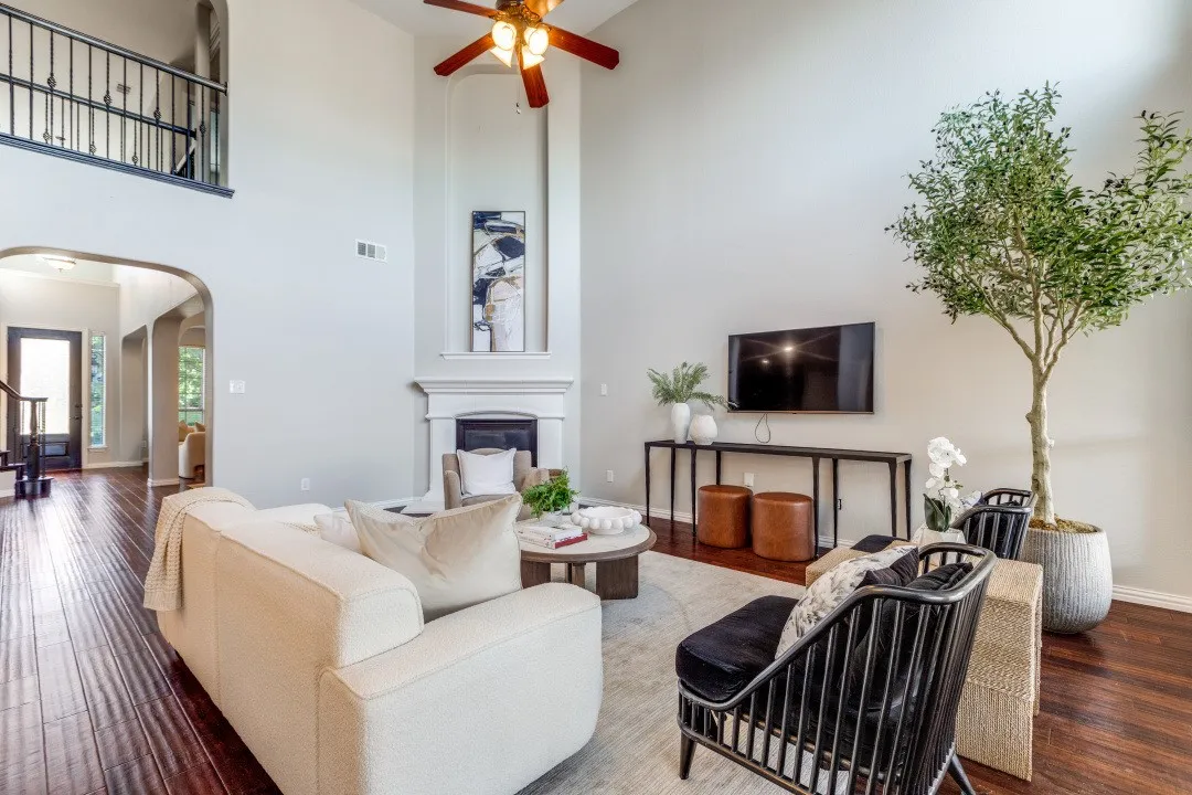 Soaring ceilings with a decorative ceiling fan, a fireplace with a mantel, dark wood-finish flooring, a second-story interior balcony with wrought iron railing, and arched doorways