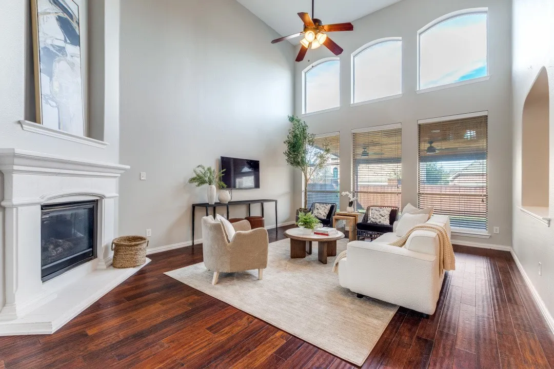 Vaulted ceiling, wood-finish flooring, fireplace with white mantel, ceiling fan, and arched window details