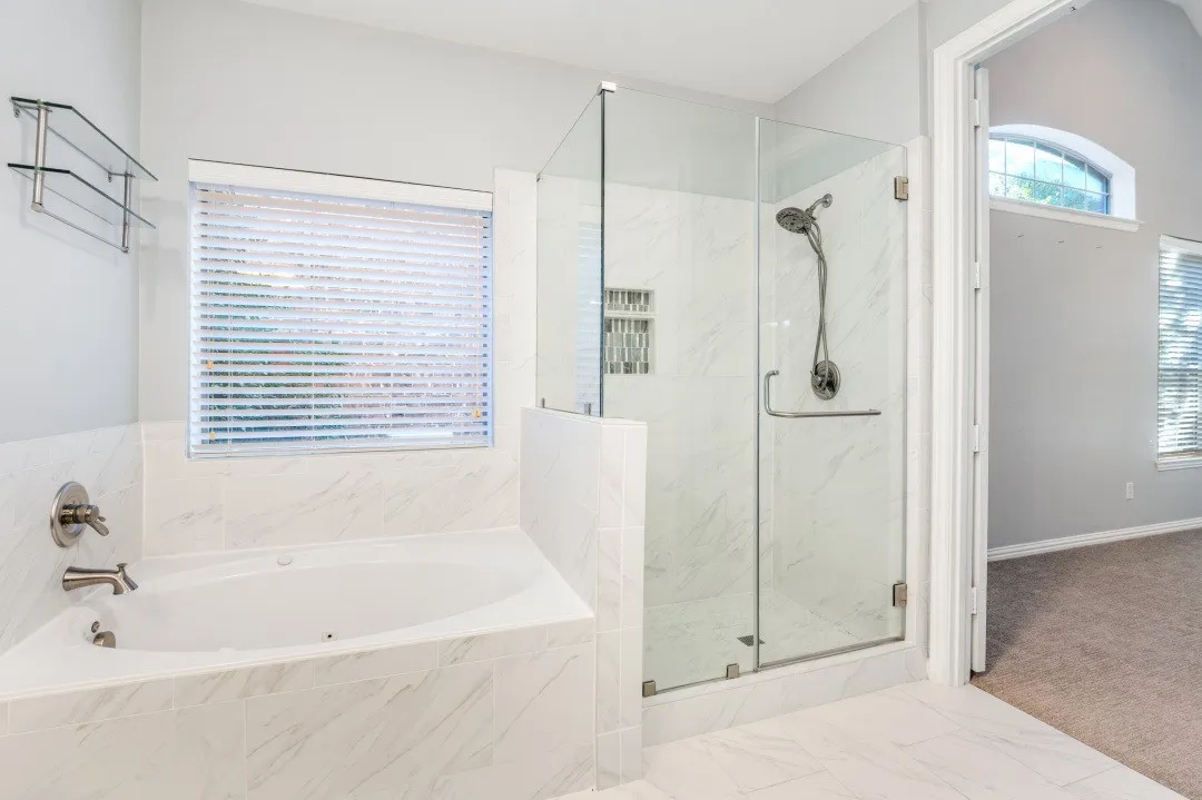 Corner soaking tub, glass-enclosed shower with tile surround, built-in shower niche, and brushed nickel fixtures