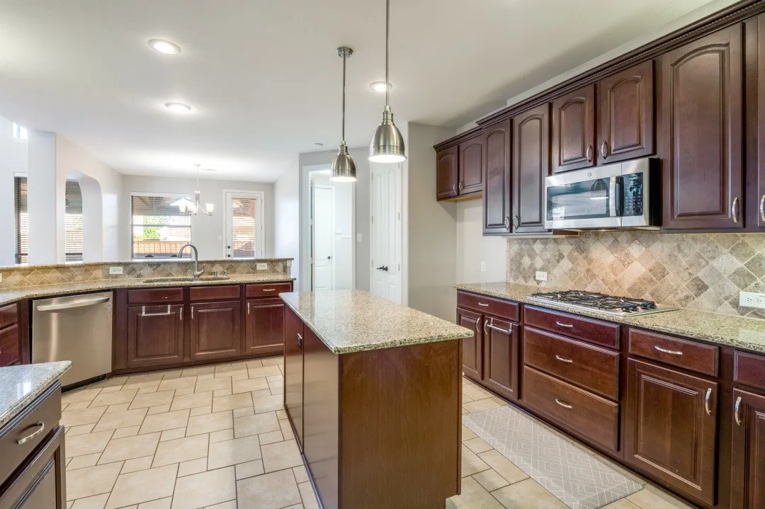 Kitchen featuring dark wood cabinetry, granite countertops, stainless steel appliances, tile backsplash, and tile flooring