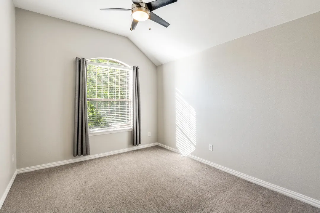 Arched window with blinds, vaulted ceiling, ceiling fan with integrated lighting, and neutral carpeting