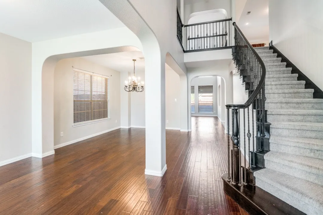 Hardwood flooring, arched doorways, chandelier lighting, carpeted staircase with wrought iron balusters, and a second-story landing