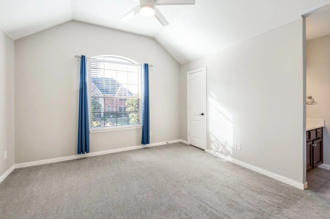 Vaulted ceiling with ceiling fan, arched window, soft gray carpeting, and a built-in vanity with dark wood-finish cabinetry