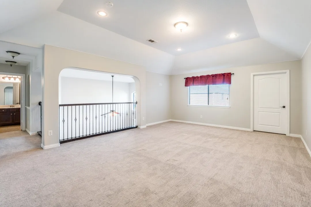 Carpeted room featuring a tray ceiling with recessed lighting, an arched doorway, and an iron baluster​​‌​​​​‌​​‌‌​‌‌​​​‌‌​‌​‌​‌​​​‌​​ railing