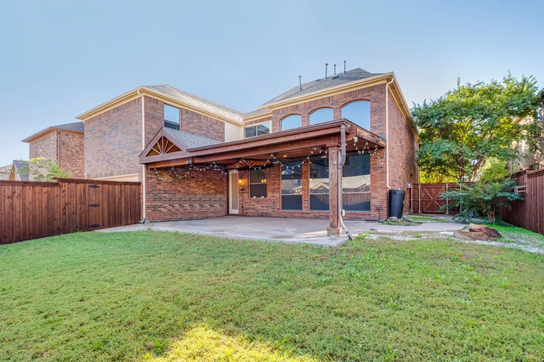 Expansive backyard featuring a brick exterior, covered patio with wood supports, and a privacy fence
