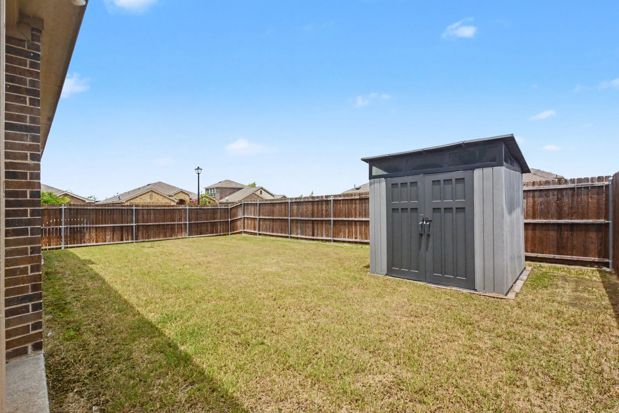 Expansive backyard featuring a manicured lawn, full privacy fencing, and a modern storage shed