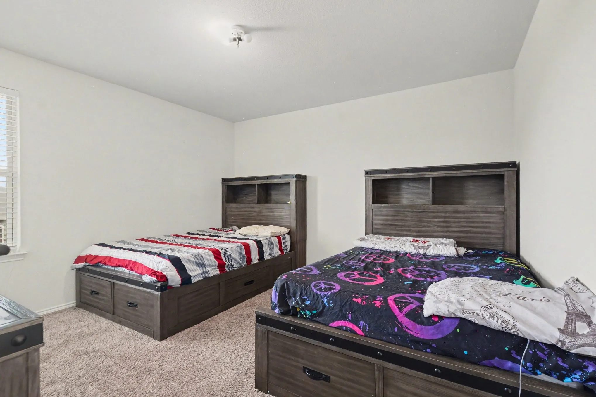 Spacious room featuring neutral wall paint, light-colored carpeting, a window with horizontal blinds, and a flush-mount ceiling light fixture