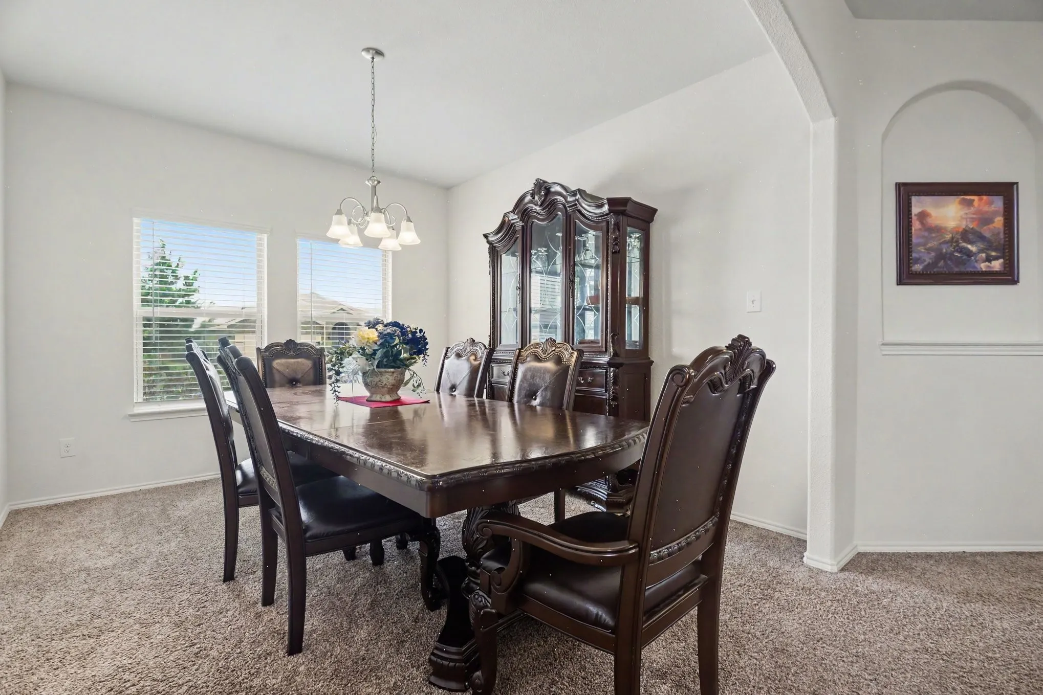 Carpeted dining area featuring two windows with blinds, a chandelier light fixture, and an arched entryway with an integrated display niche