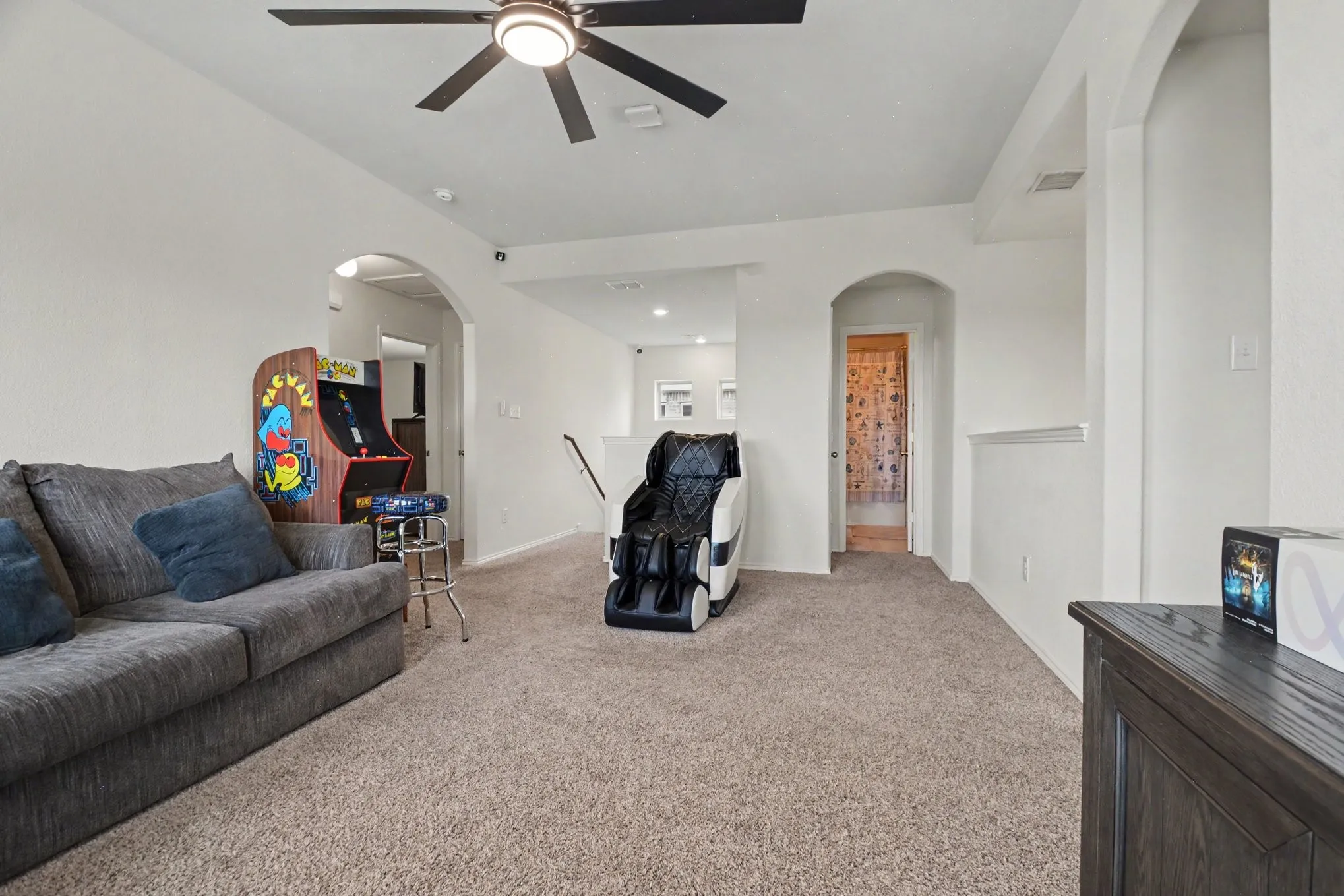 Spacious carpeted room featuring a ceiling fan with integrated lighting, multiple arched doorways, and light-toned wall finishes