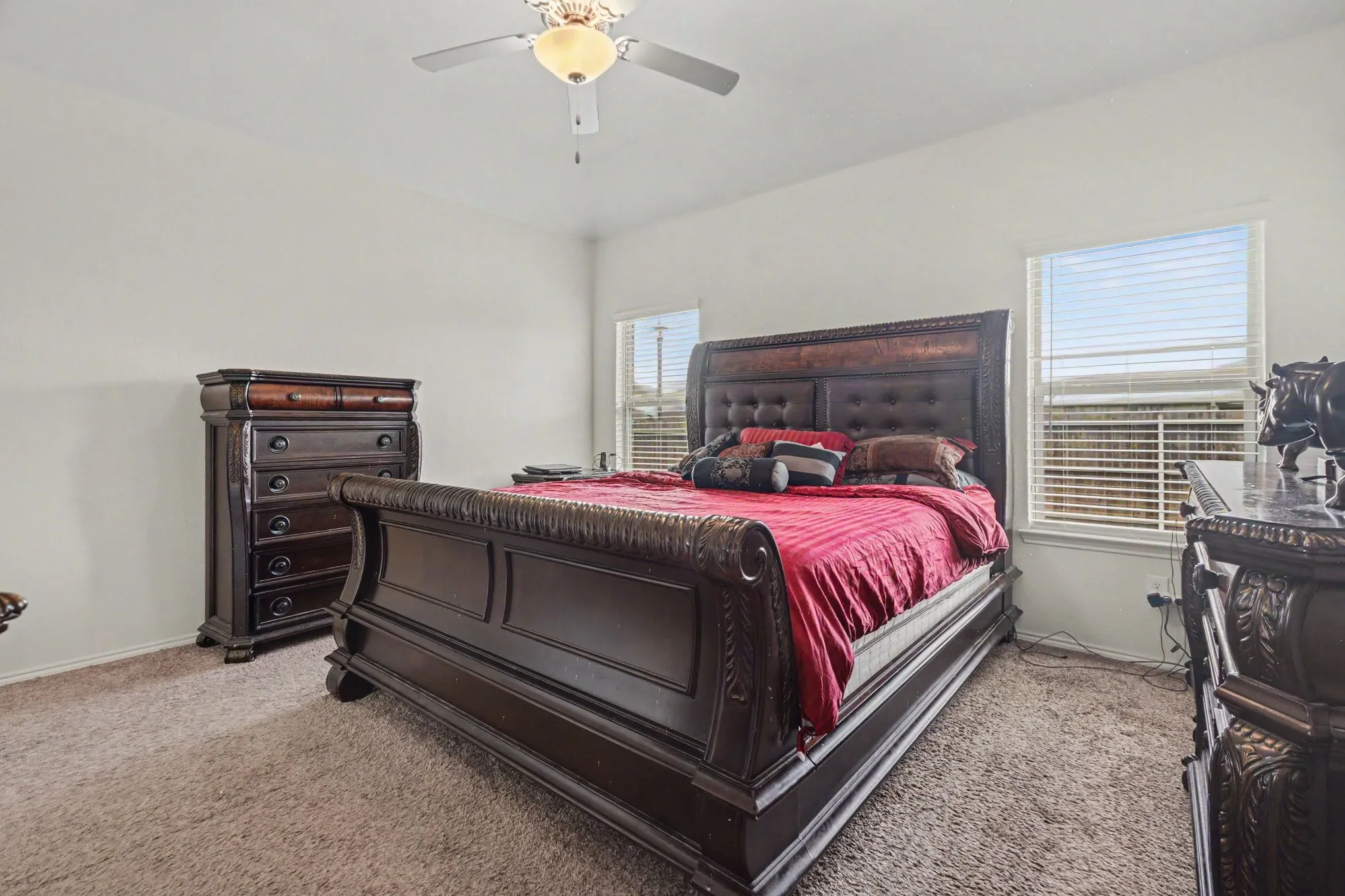 Carpeted bedroom with neutral wall paint, featuring a ceiling fan with integrated lighting, and two windows with horizontal blinds