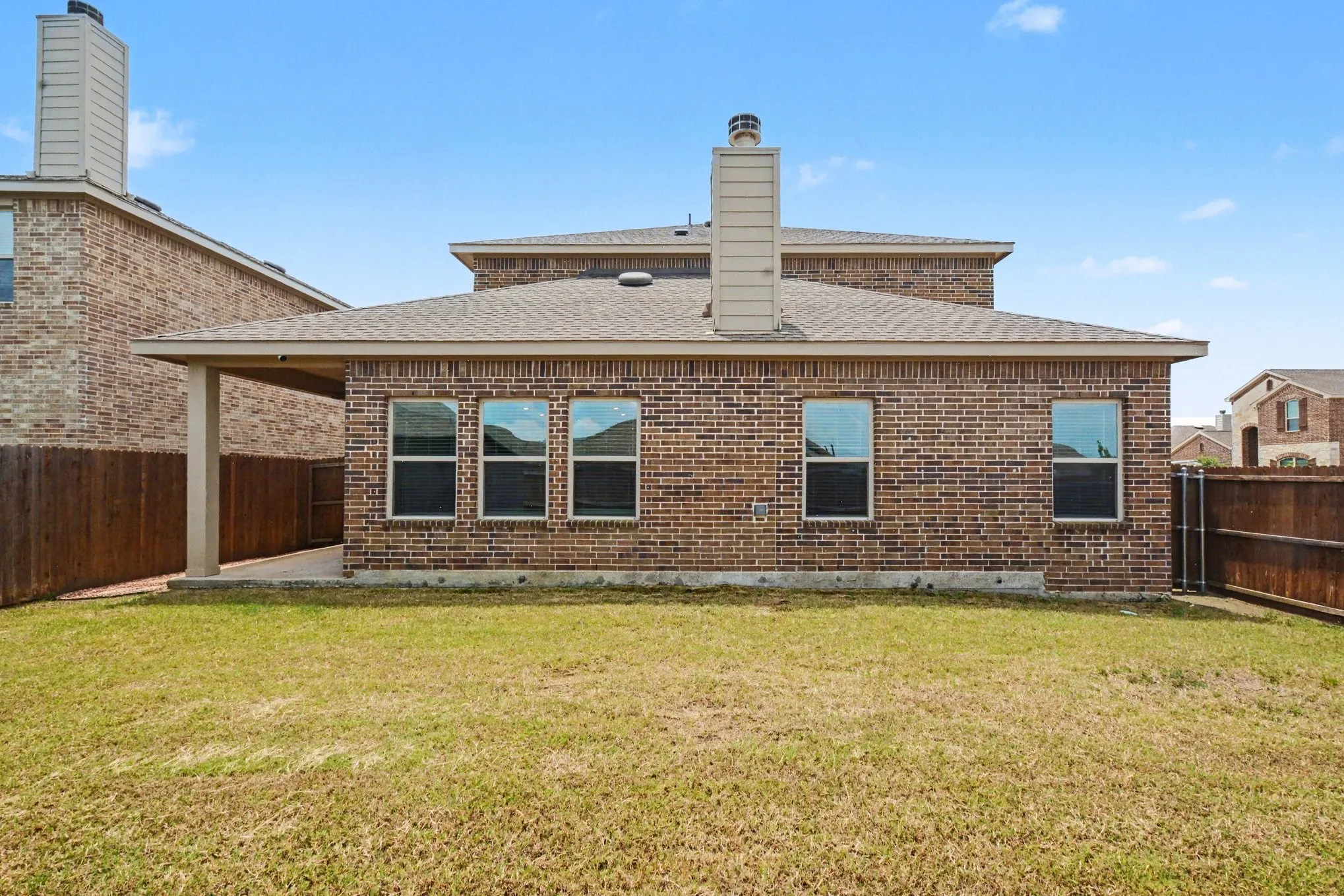 Rear exterior featuring a brick facade, covered patio, multiple windows, a shingled roof, and a privacy fence