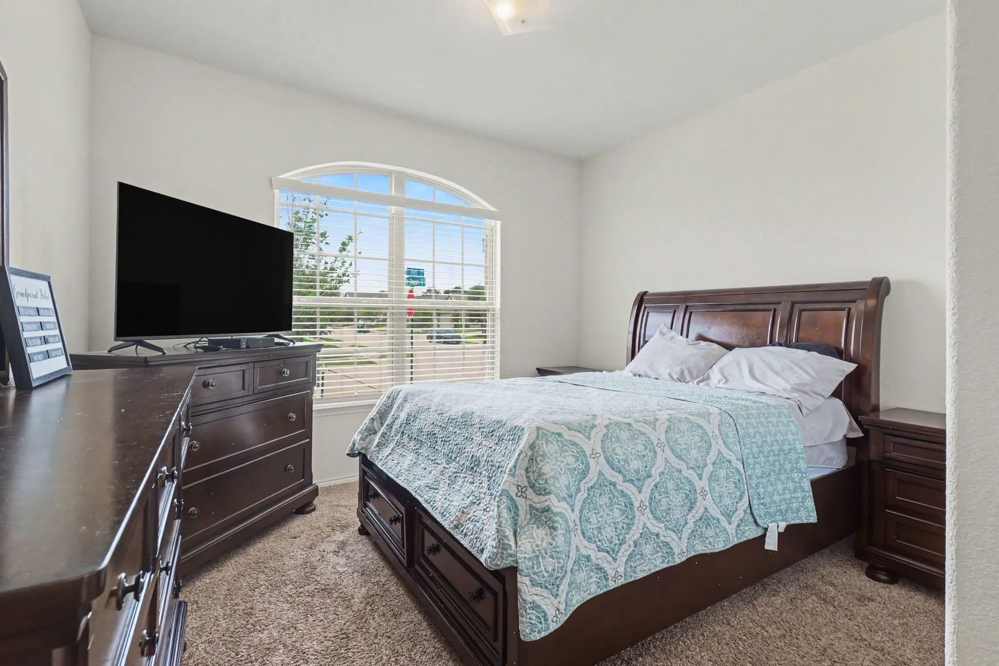 Bedroom featuring a large arched window with blinds, light-toned walls, and carpet flooring