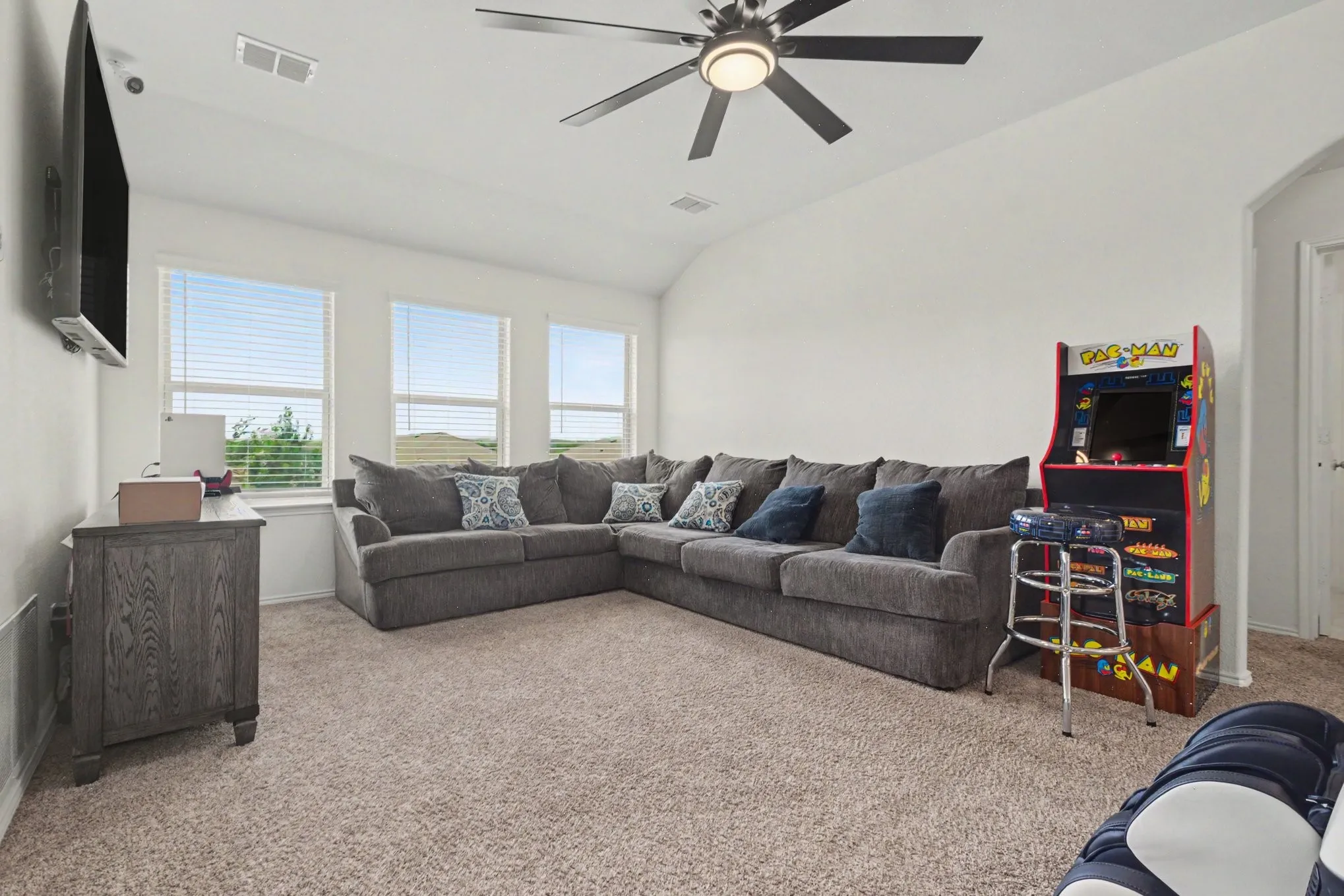 Carpeted room featuring multiple windows with blinds, a vaulted ceiling, and a ceiling fan with integrated lighting