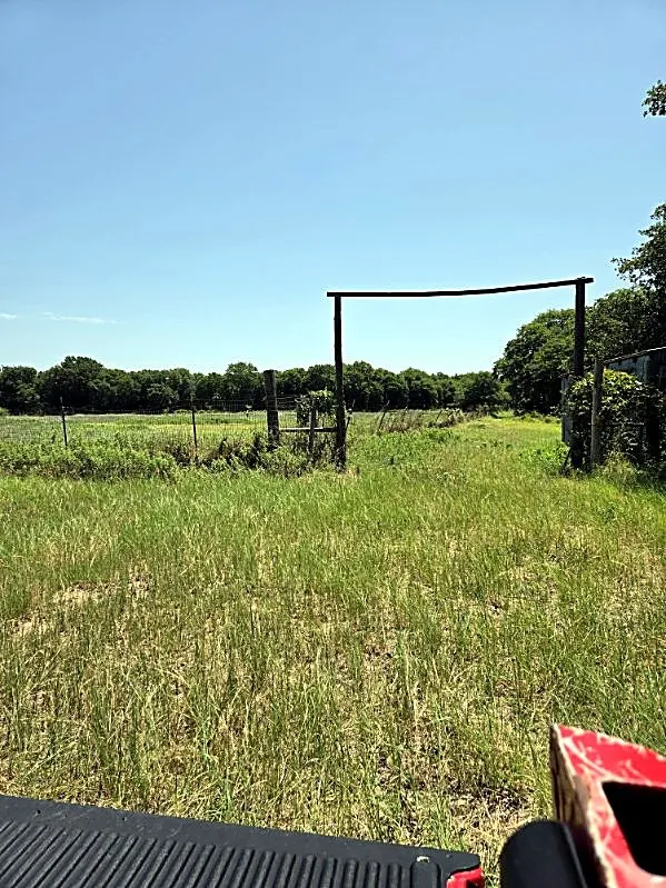 Expansive grassy terrain with a distant tree line and a rustic wood gate frame