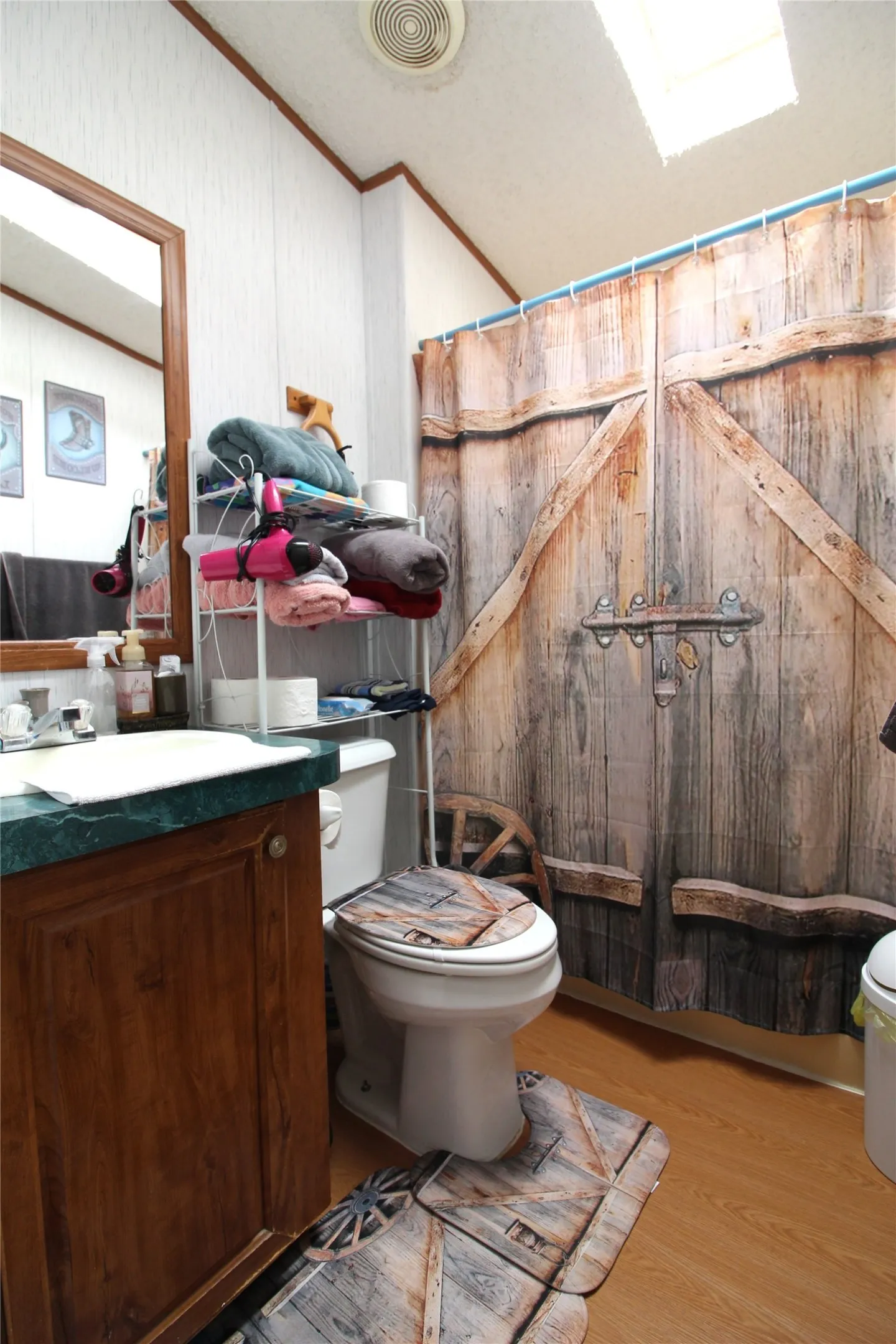 Bathroom featuring a wood-finish vanity with integrated sink, wood-finish flooring, a skylight for natural illumination, and a barn-door-style shower enclosure with rustic wood detailing and metal hardware