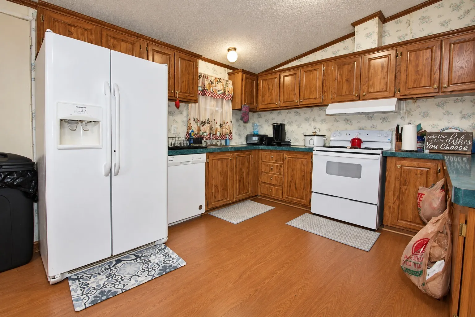 Wood-finish flooring, ample wood cabinetry, side-by-side refrigerator, built-in dishwasher, and a white range with overhead ventilation
