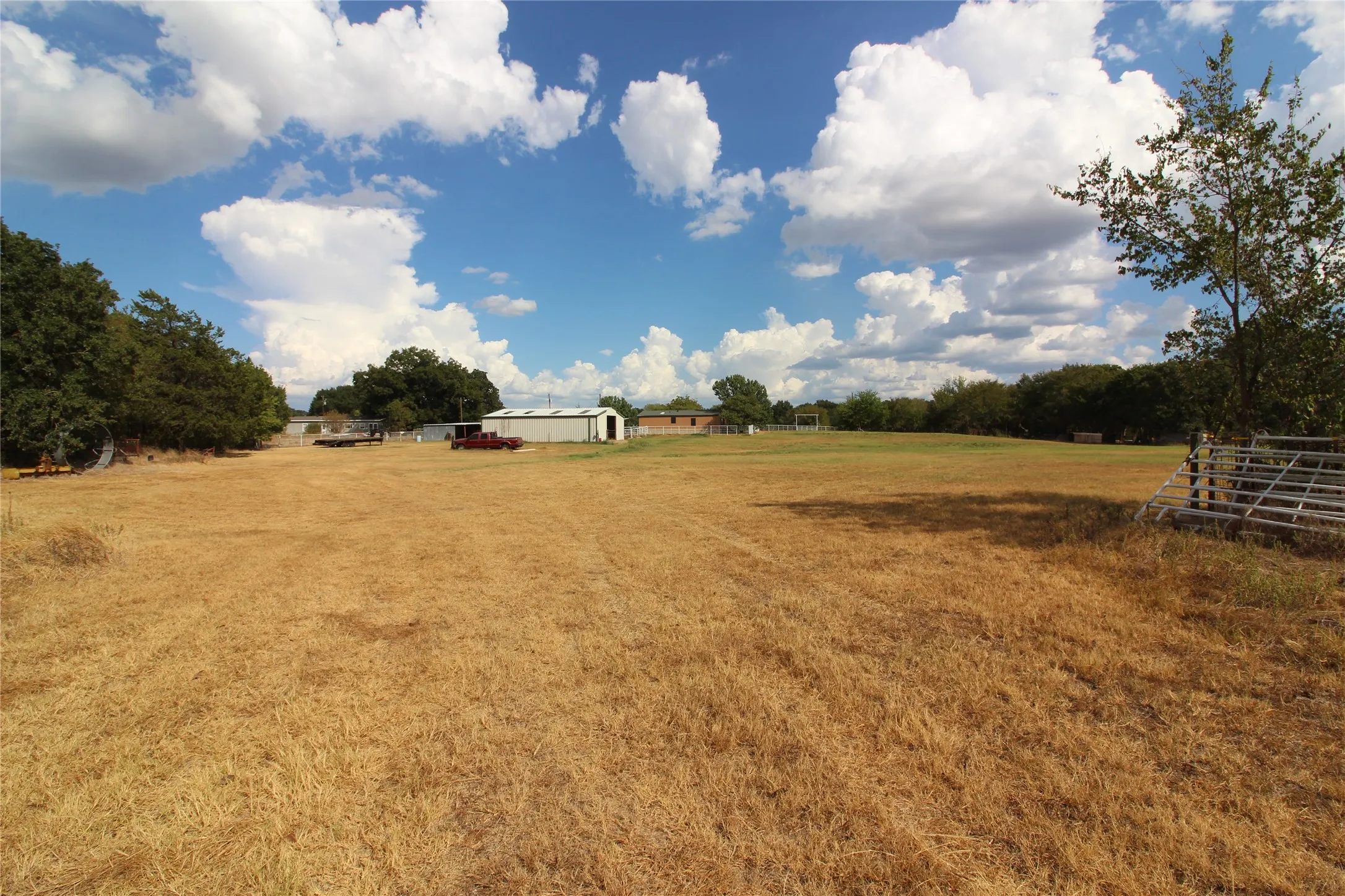 Expansive land featuring a metal building, a single-story structure, and scattered trees