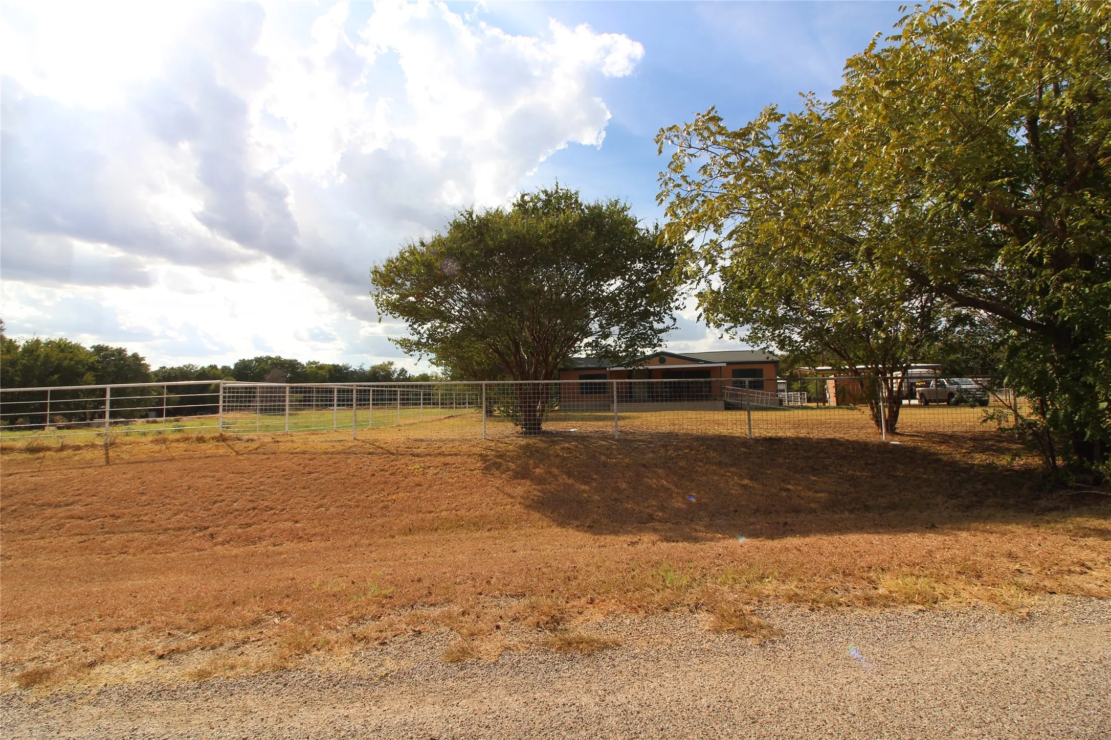 Extensive fenced perimeter with a gravel foreground and mature trees