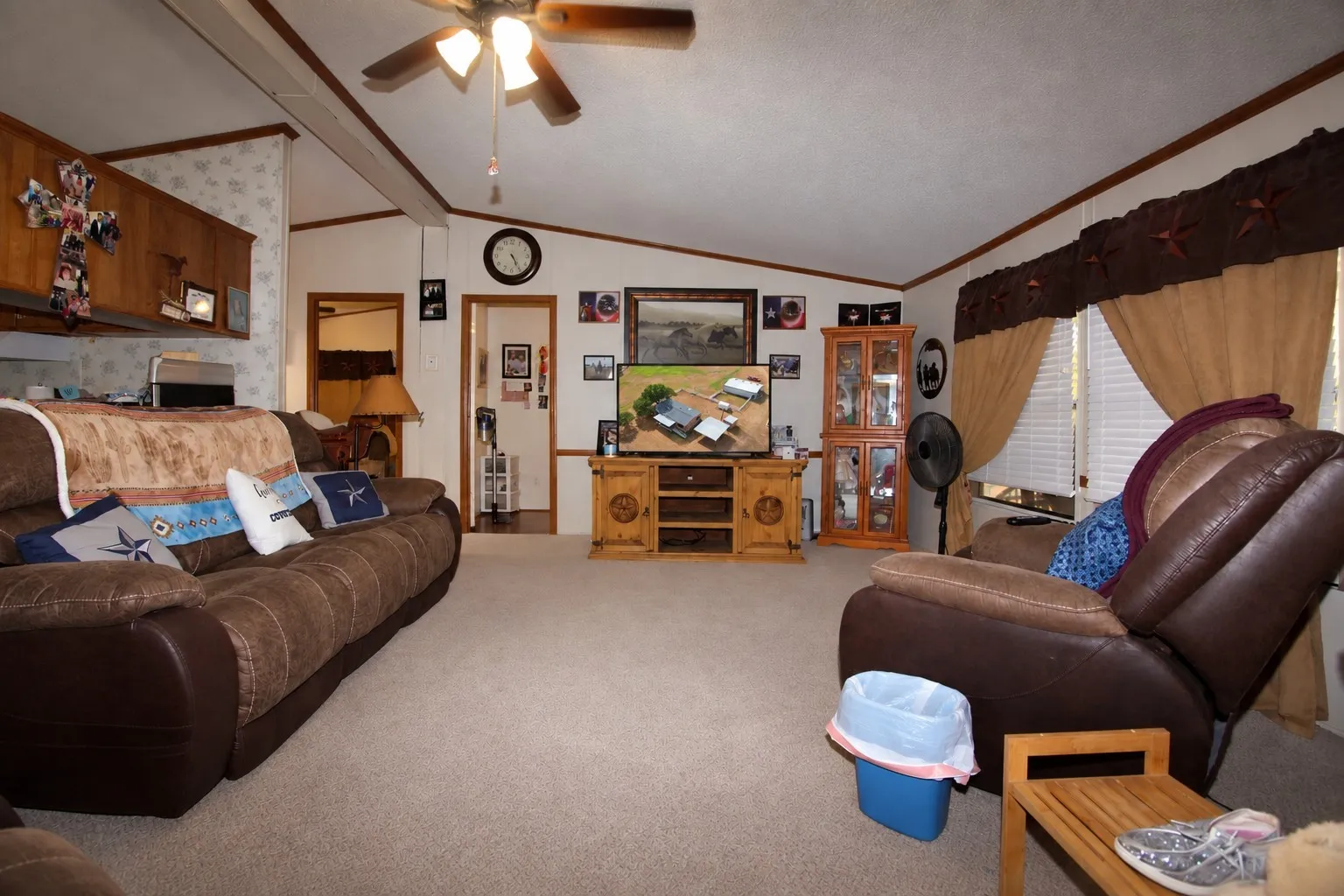 Carpeted living area featuring a ceiling fan, wood trim accents, and natural light from a window with blinds