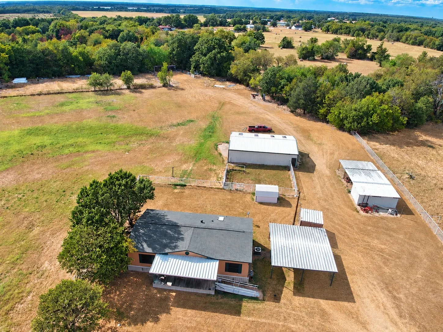 Expansive property featuring a main residence with a covered porch, a large detached workshop, an open-sided shed, a standalone storage shed, and mature trees