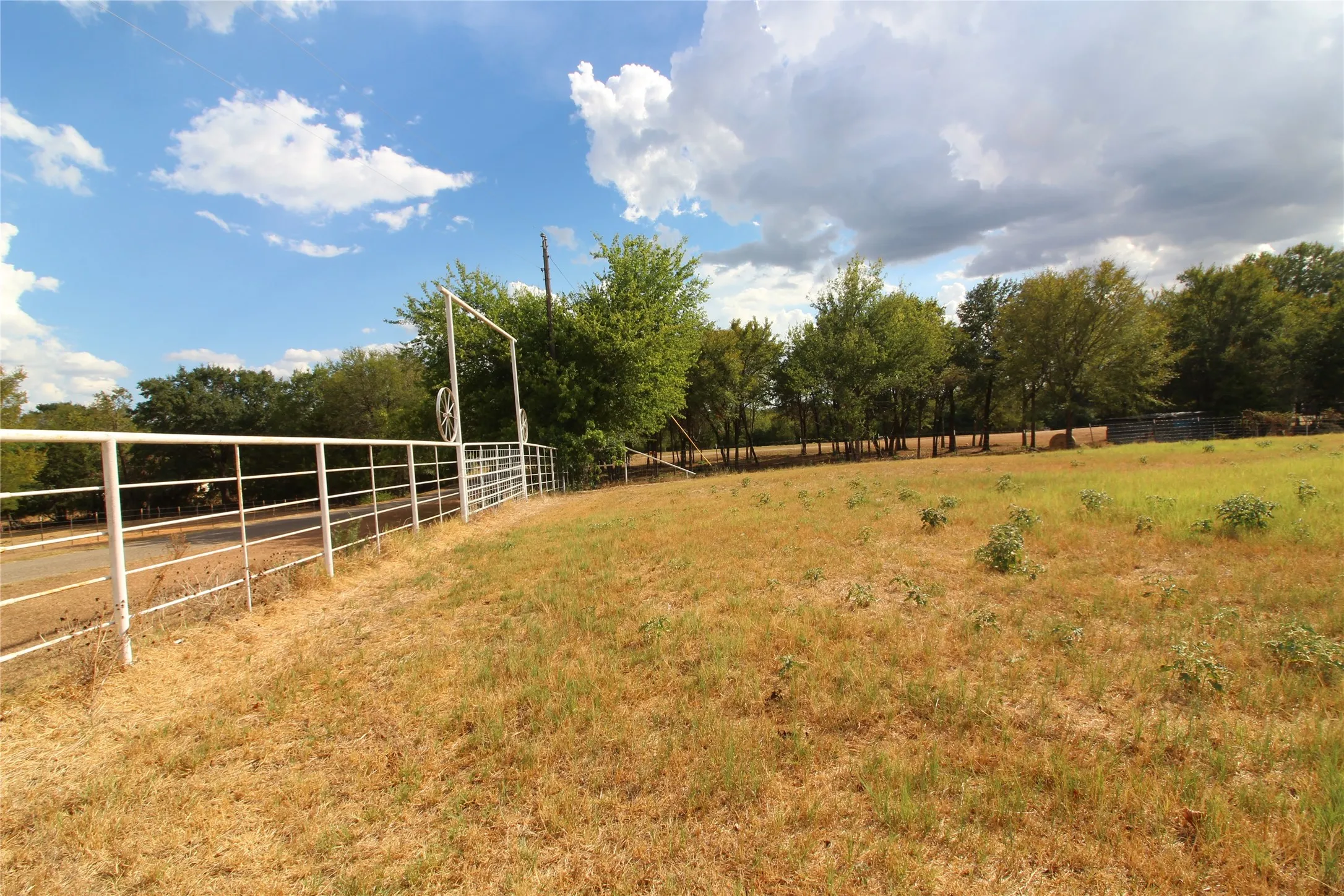 Expansive open land featuring a white metal perimeter fence and mature trees
