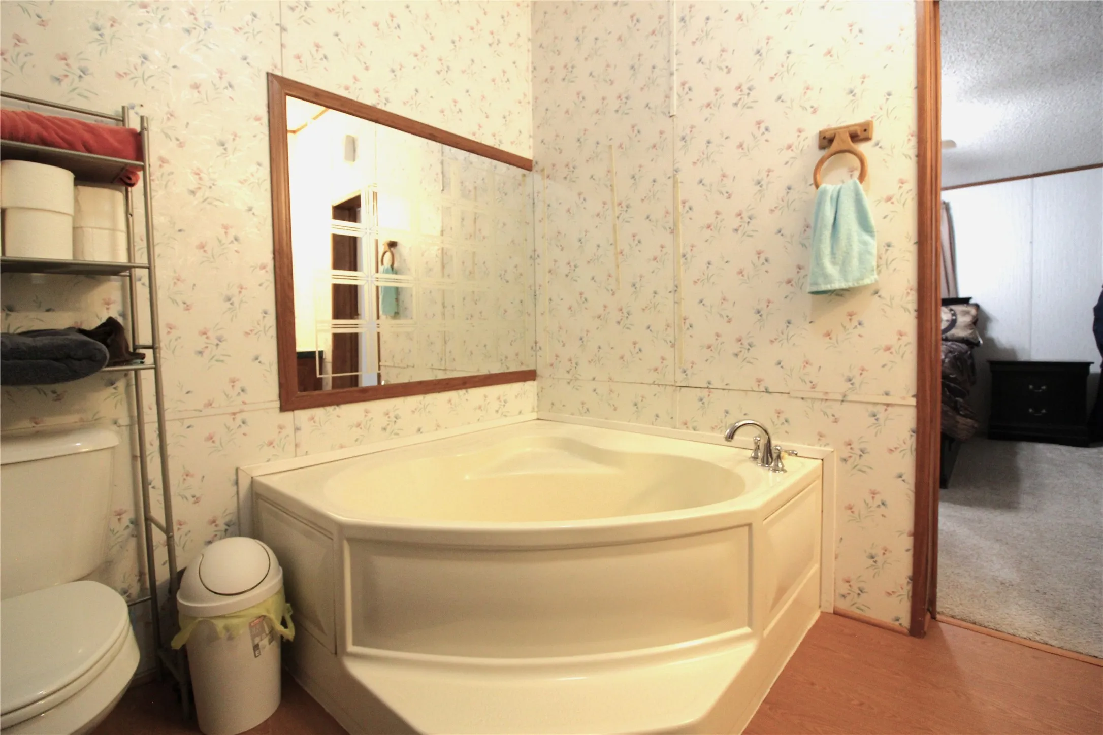 Corner soaking tub with polished chrome fixtures and wood-finish flooring