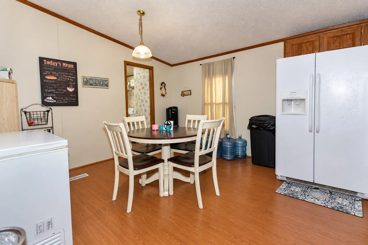Wood-finish flooring throughout, white walls with wood trim, and a window with sheer curtains