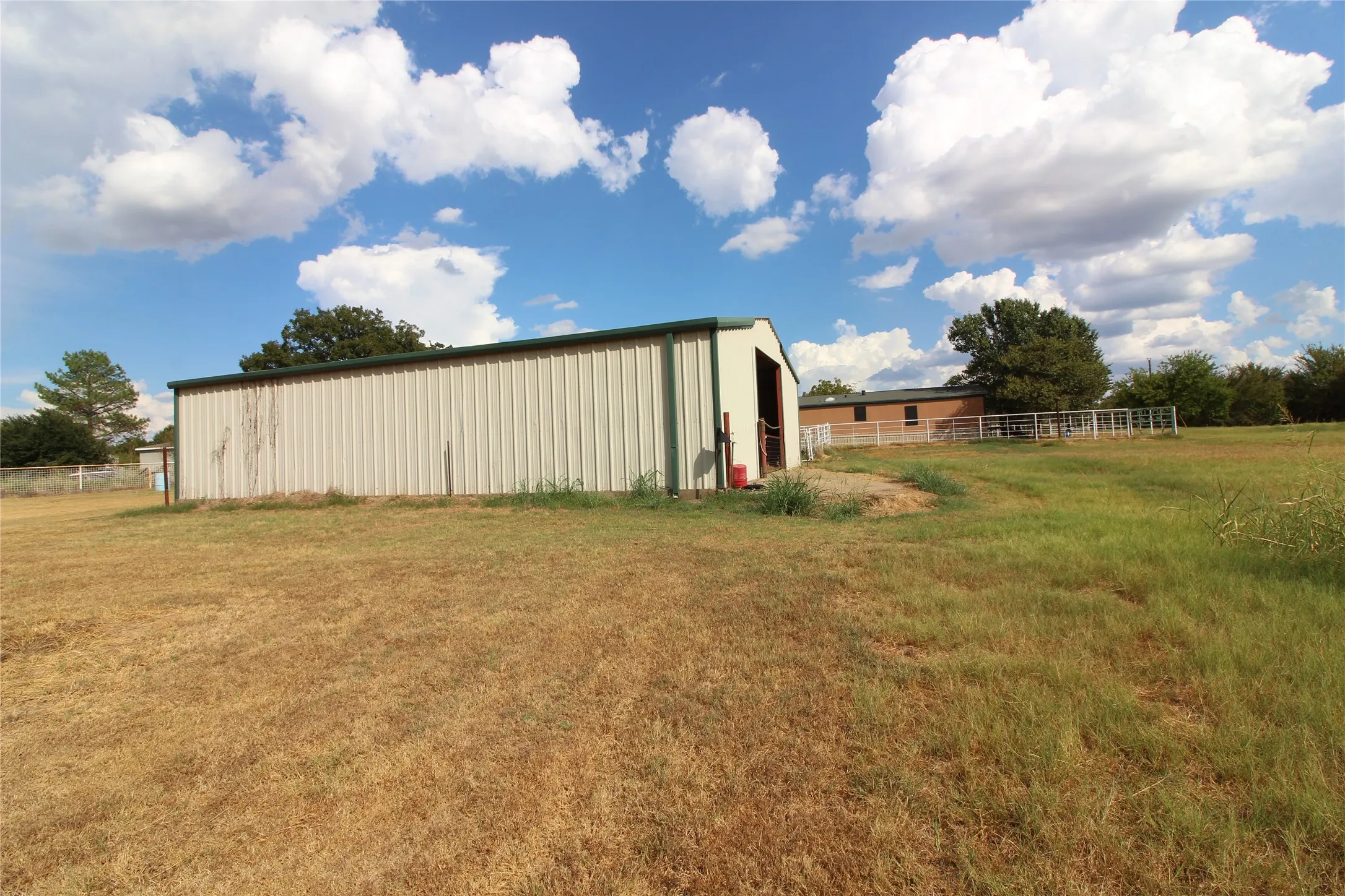Metal utility building with a green trim roof, expansive grassy area, and a fenced enclosure