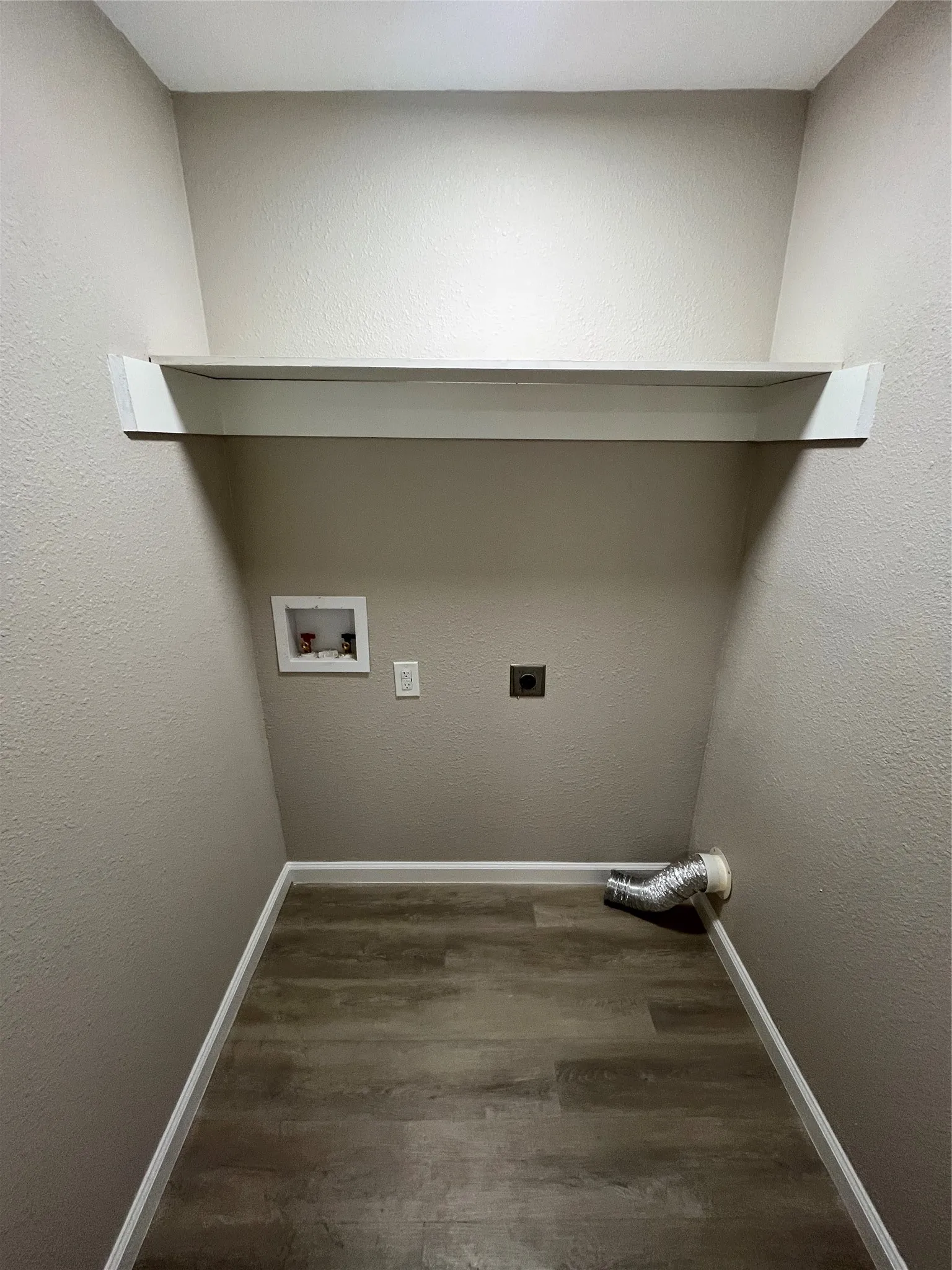 Laundry area featuring wood-finish flooring, a built-in white shelf, and light-toned walls