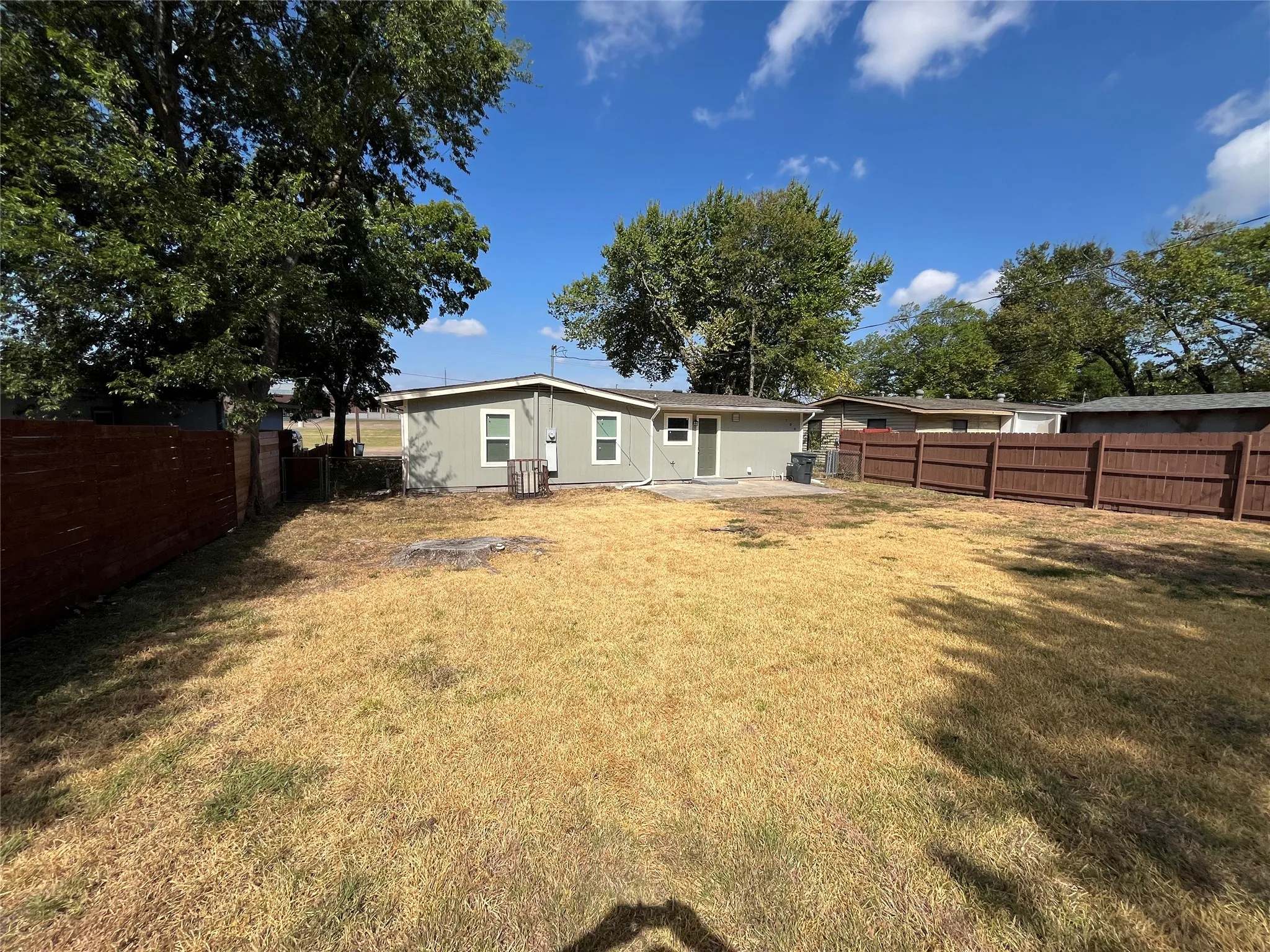 Expansive backyard with a full perimeter fence, mature trees, and a concrete patio