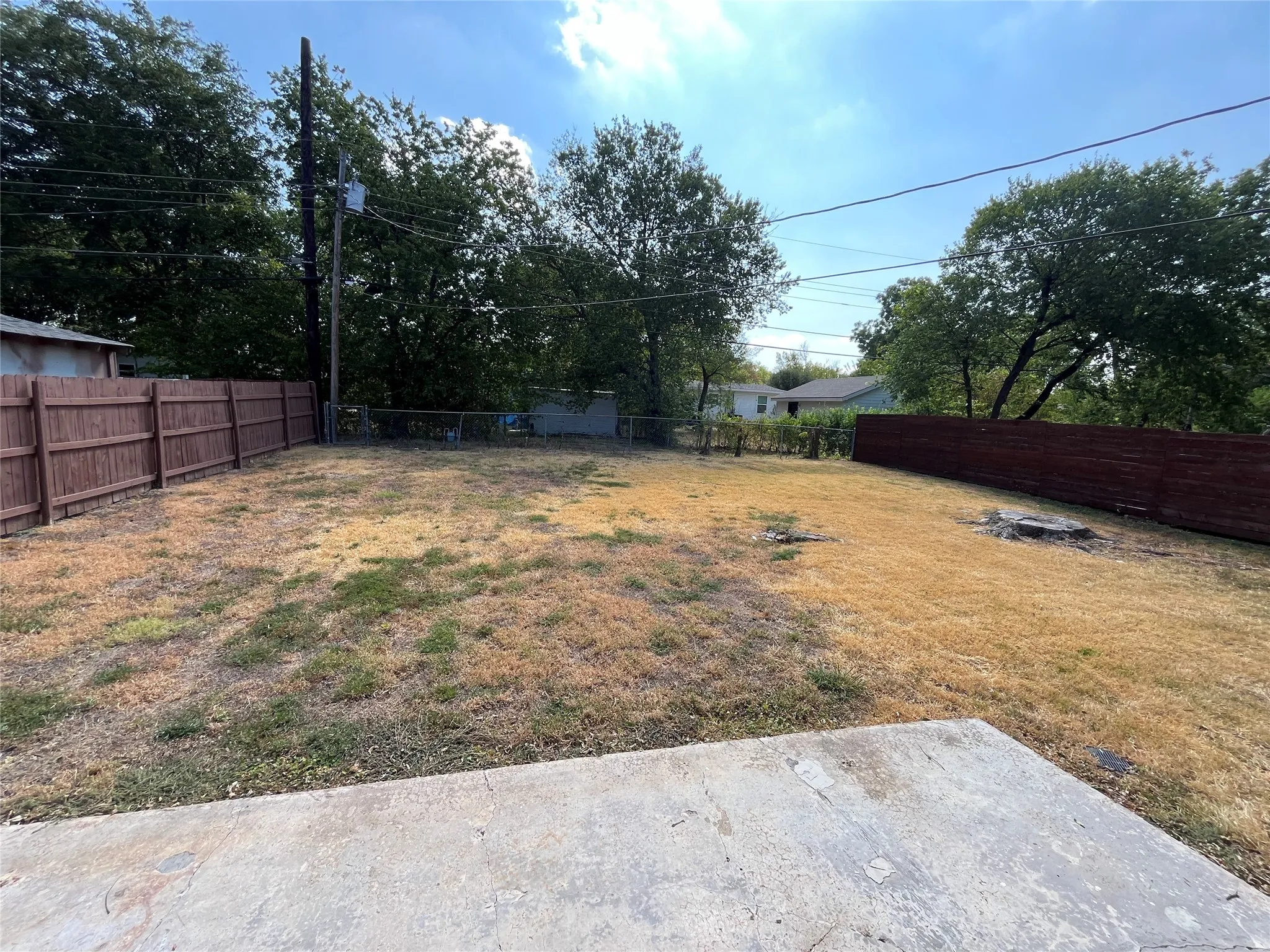 Expansive backyard with a concrete patio, wood privacy fencing, and mature trees