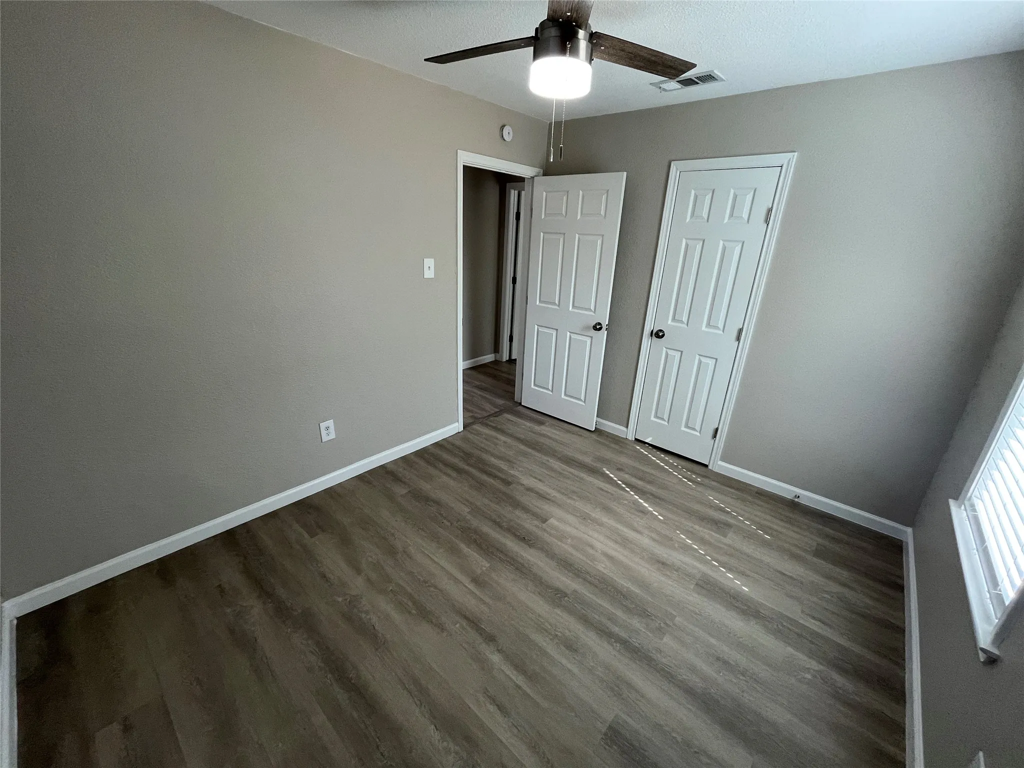 Wood-finish flooring, neutral wall color, ceiling fan with integrated lighting, window with blinds
