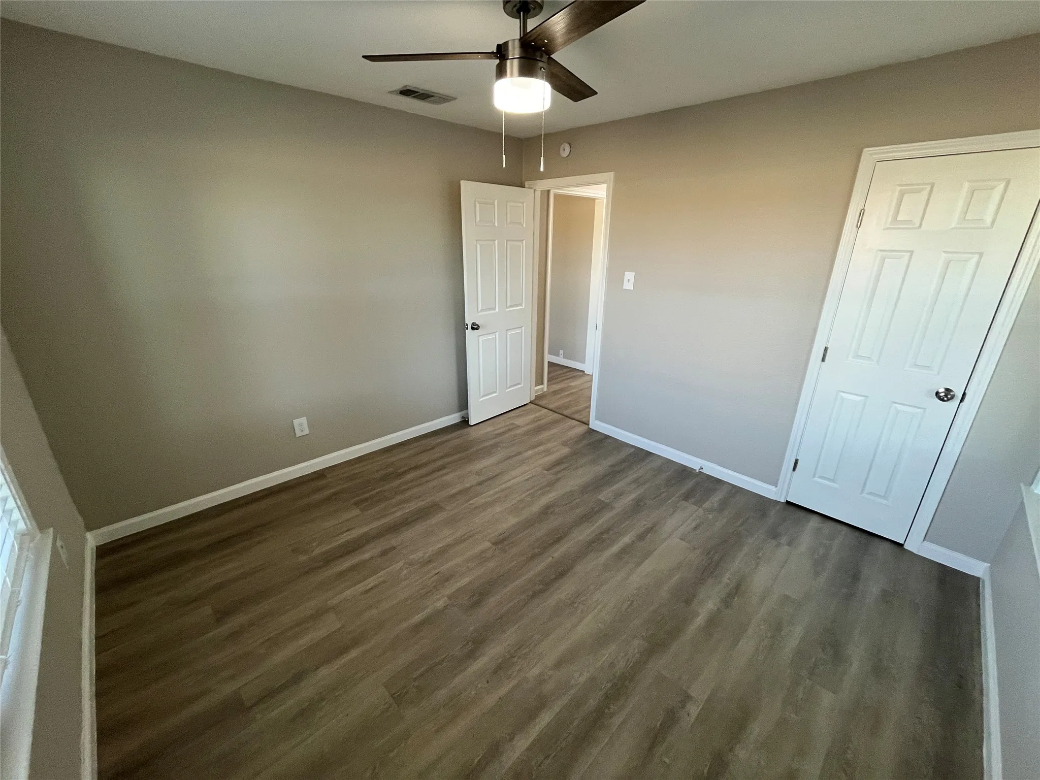 Wood-finish flooring, neutral wall tones, ceiling fan with integrated lighting, and white paneled doors