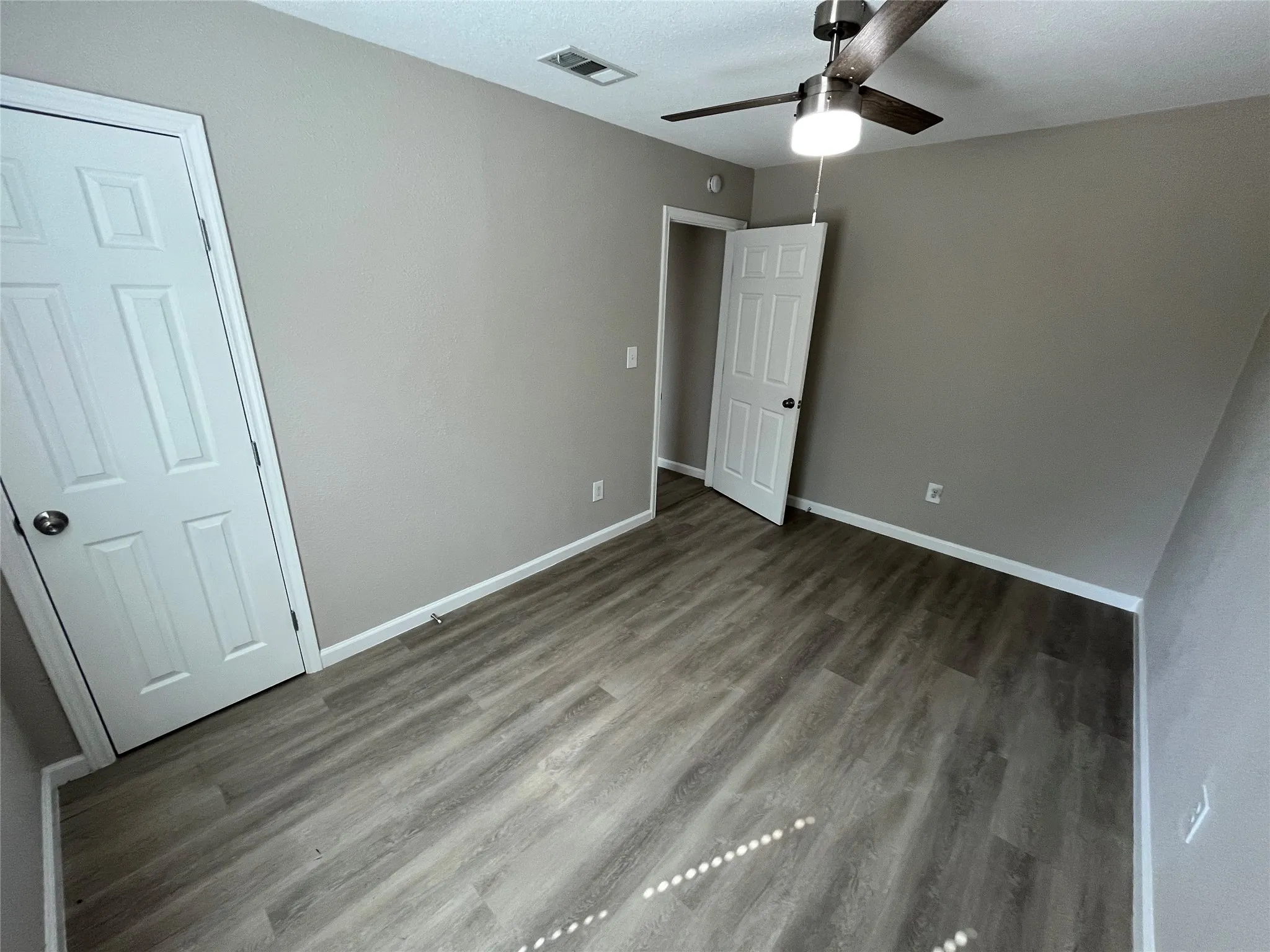 Wood-finish flooring, neutral wall color, ceiling fan with integrated lighting, and white paneled doors